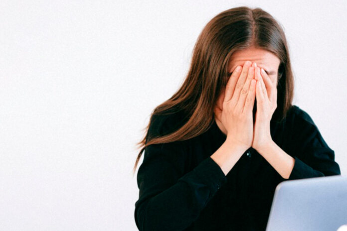 Mujer desesperada, con cara tapada frente a notebook.